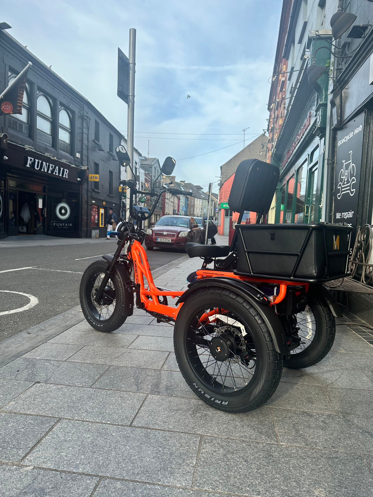 Side rear view of the orange Meet One Tour 2.0 e-trike in the city.
